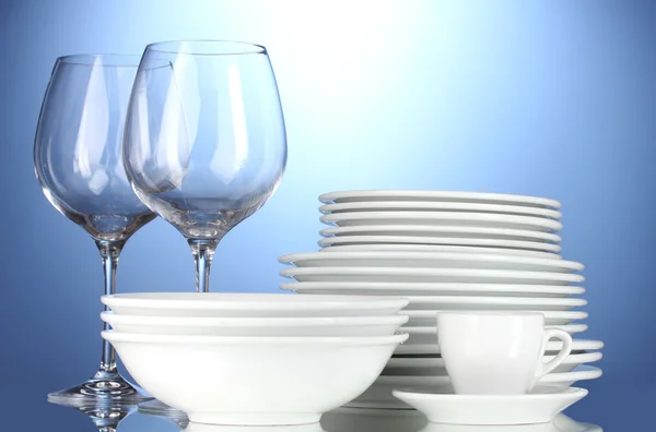 Bols vides, assiettes, tasses et verres sur fond bleu — Photo