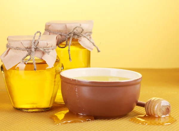 Jars of honey, bowl and wooden drizzler with honey on yellow honeycomb background — Stock Photo, Image