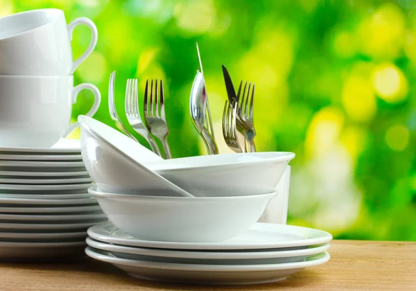 stock image Clean dishes on wooden table on green background