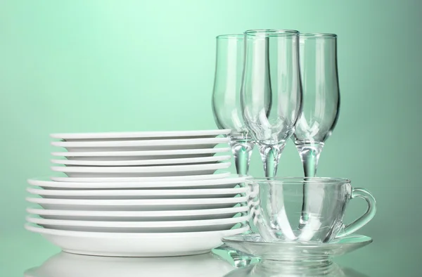 Czyste talerze, szklanki i okulary na zielonym tle — Zdjęcie stockowe