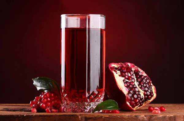 Pomergranato maturo e bicchiere di succo su tavolo di legno su sfondo rosso — Foto Stock
