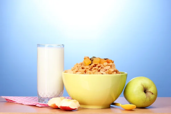 在绿色碗、 苹果和一杯牛奶在蓝色背景上的木桌上的美味玉米片 — 图库照片