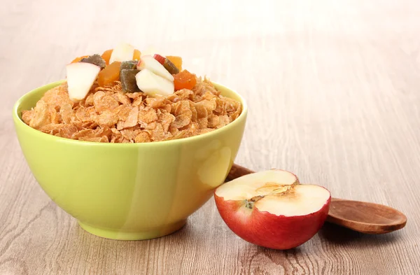 Leckere Cornflakes in Schüssel mit getrockneten Früchten und Apfel auf Holztisch — Stockfoto