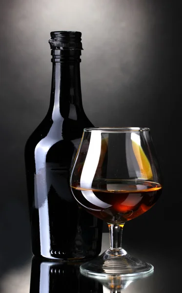Glass of brandy and bottle on gray background — Stock Photo, Image