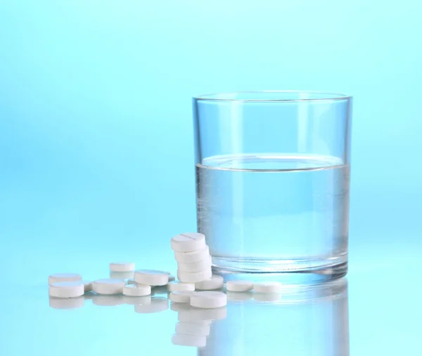 Glas water en pillen op blauwe achtergrond — Stockfoto