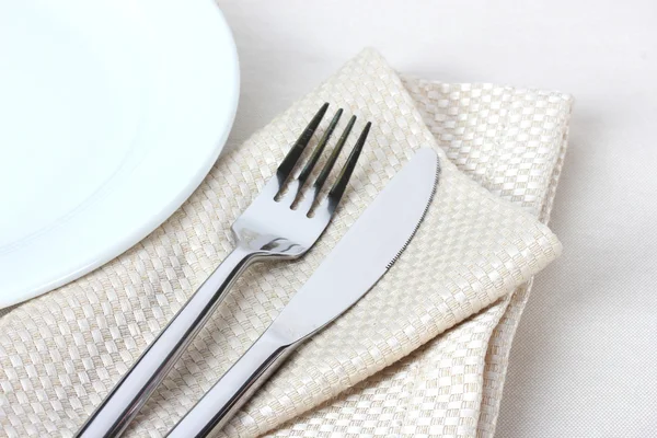 Вилка, нож на салфетке и тарелка изолированы на белом — стоковое фото