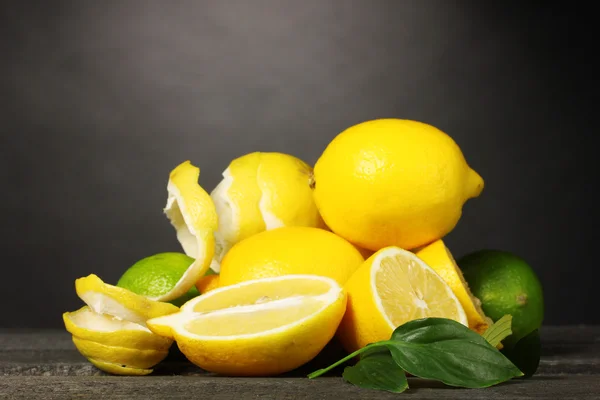 Спелые лимоны и лаймы с листьями на деревянном столе на сером фоне — стоковое фото