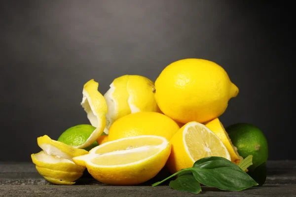 Limoni maturi e lime con foglie su tavola di legno su fondo grigio — Foto Stock