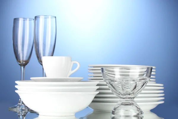 Ciotole vuote, piatti, tazze e bicchieri su sfondo blu — Foto Stock