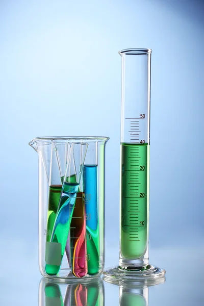 Naczynia laboratoryjne z kolor płynu i odbicie na niebieskim tle — Zdjęcie stockowe