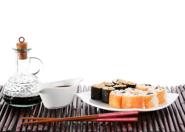 Вкусные булочки подаются на белой тарелке с палочками для еды и соевым соусом на бамбуковом коврике, изолированном на белом — стоковое фото