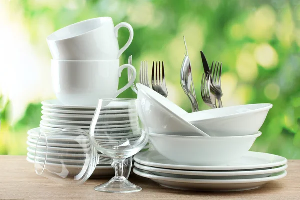 Czyste naczynia na drewnianym stole na zielonym tle — Zdjęcie stockowe