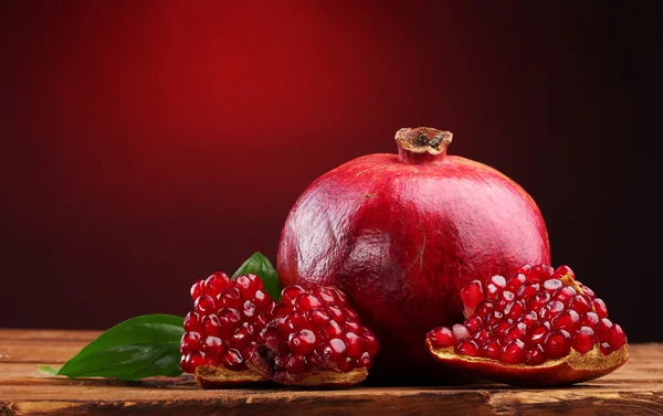 Ripe pomegranate fruit with leaves on wooden table on red background — Stock Photo, Image