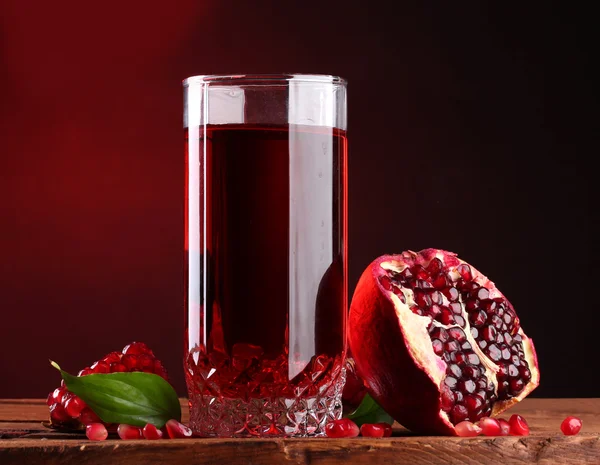 Ripe pomergranate and glass of juice on wooden table on red background — Stock Photo, Image