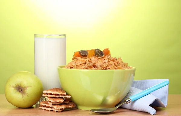 Välsmakande cornflakes i grön skål, äpple och glas mjölk på träbord på grön bakgrund — Stockfoto