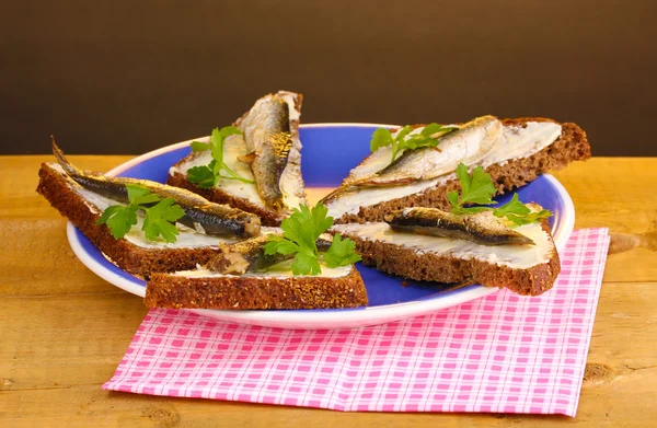 stock image Tasty sandwiches with sprats on plate on wooden table on brown background