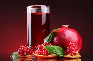 Ripe pomergranate and glass of juice on red background clipart