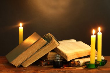 Old books, scrolls, ink pen inkwell and candles on wooden table on brown background clipart