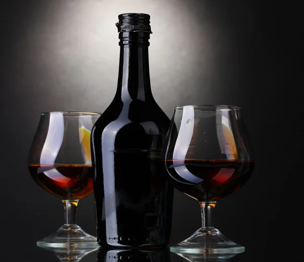Brýle brandy a láhev na šedém pozadí — Stock fotografie