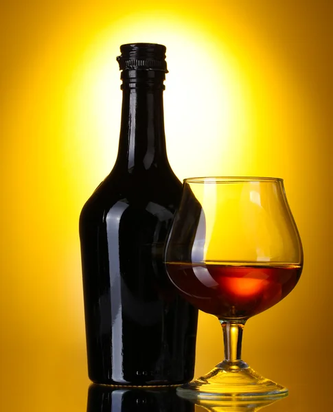 Bicchiere di brandy e bottiglia su sfondo giallo — Foto Stock