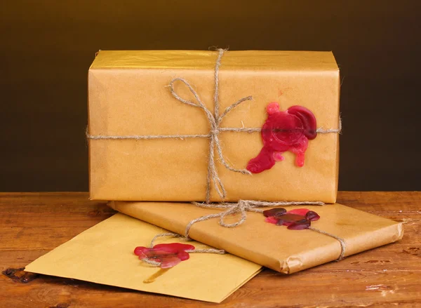 Посылки и конверт с герметичным воском на деревянном столе на коричневом фоне — стоковое фото