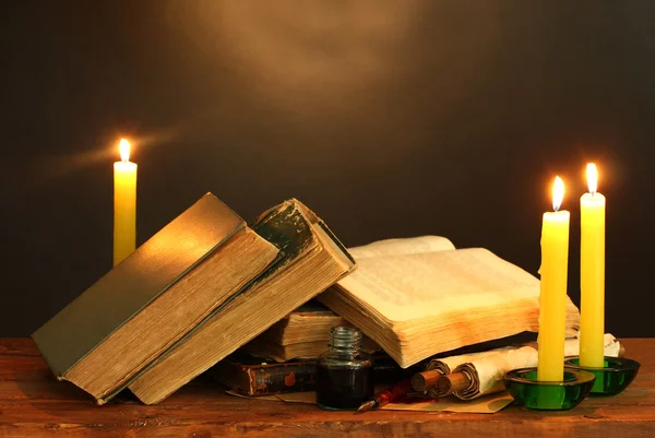 Oude boeken, rollen, inkt pen inktpotje en kaarsen op houten tafel op bruine achtergrond — Stockfoto