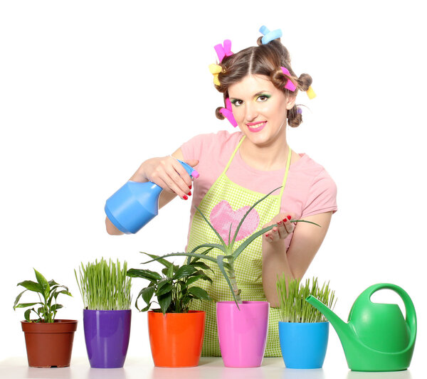 Beautiful happy young housewife sprays plants in flowerpots isolated on white