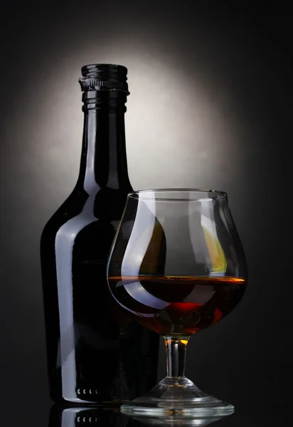Glass of brandy and bottle on gray background — Stock Photo, Image