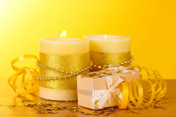 Hermosas velas y regalos en mesa de madera sobre fondo amarillo —  Fotos de Stock