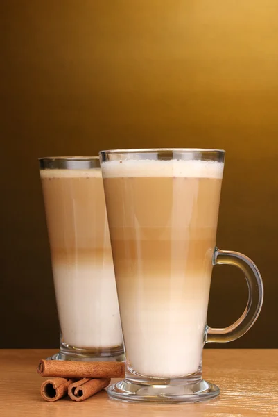 Fragrante latte macchiato in tazza di vetro e cannella su tavolo di legno su sfondo marrone — Foto Stock