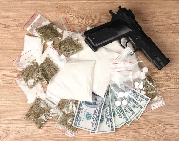 Кокаїн і марихуана в упаковках, доларах і пістолеті на дерев'яному фоні — стокове фото