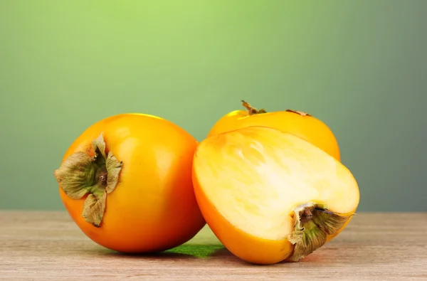 stock image Appetizing persimmons on wooden table on green background