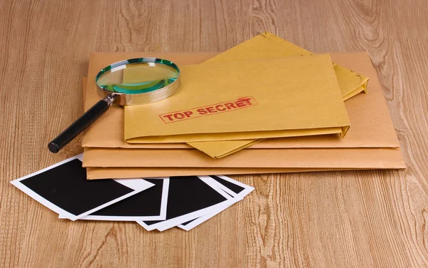 Kuvert med topp hemlig stämpel med fotopapper och förstoringsglas på trä bakgrund — Stockfoto