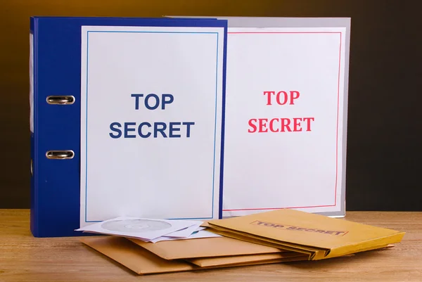 Enveloppen en mappen met top geheime stempel en cd schijven op houten tafel op bruine achtergrond — Stockfoto