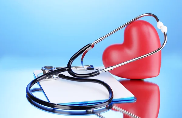 Medizinisches Stethoskop mit Klemmbrett und Herz auf blauem Hintergrund — Stockfoto