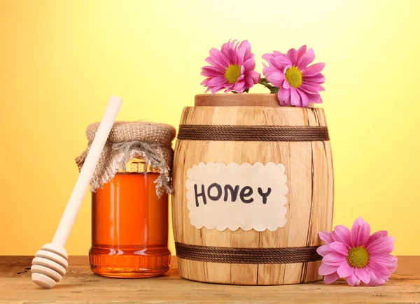 Miel dulce en barril y tarro con rociador sobre mesa de madera sobre fondo amarillo —  Fotos de Stock