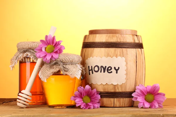 Sweet honey in barrel and jars with drizzler on wooden table on yellow background — Stock Photo, Image