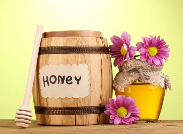 Süßer Honig in Fass und Glas mit Nieselregen auf Holztisch auf grünem Hintergrund — Stockfoto