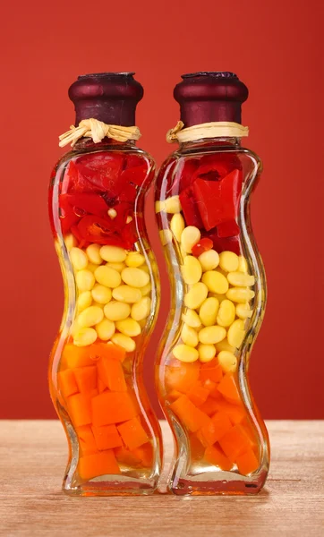 Dvě láhve s červenou paprikou, fazole, mrkev pro výzdobu kuchyně na červeném pozadí — Stock fotografie