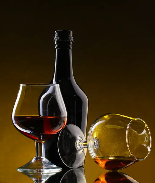 Glasses of brandy and bottle on yellow background — Stock Photo, Image