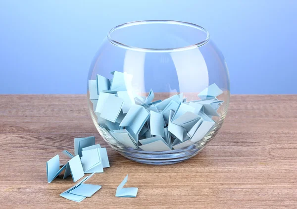 Kousky papíru pro loterie v váza na dřevěný stůl na modrém pozadí — Stock fotografie