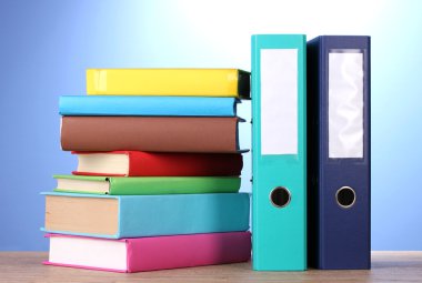 Bright office folders and books on wooden table on blue background clipart