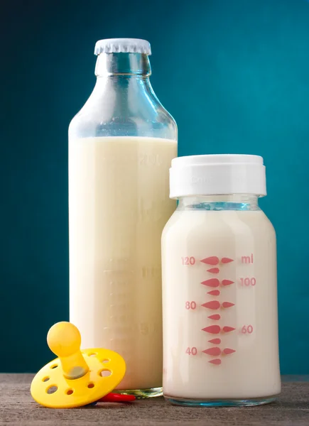 Flaskor av mjölk och nappen på träbord på blå bakgrund — Stockfoto