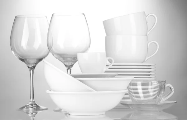 Tomma skålar, tallrikar, muggar och glas på grå bakgrund — Stockfoto