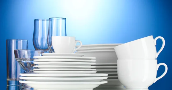 Üres tálak, tányérok, poharak és csészék a kék háttér — Stock Fotó