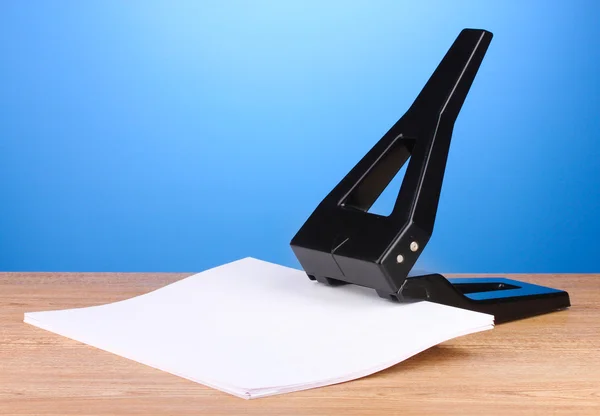 Buraco negro escritório perfurar com papel sobre fundo azul — Fotografia de Stock