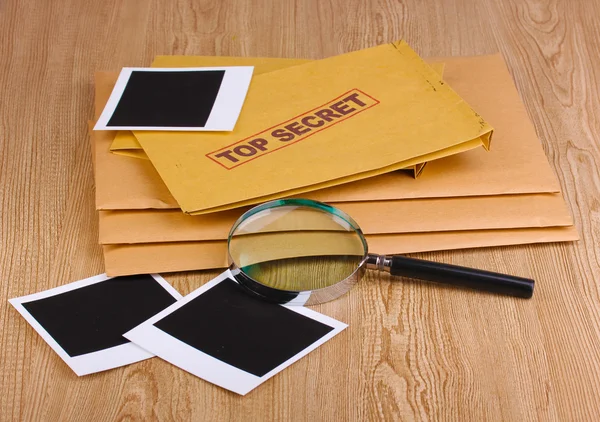Φάκελοι με κορυφαίο μυστικό σφραγίδα με φωτογραφικά χαρτιά και μεγεθυντικό φακό σε ξύλινα φόντο — Φωτογραφία Αρχείου