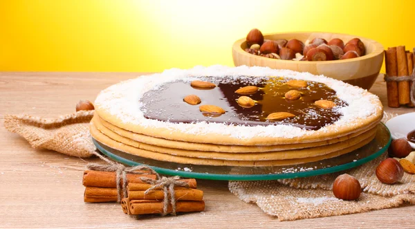 Торт на стеклянном стенде и орехи на деревянном столе на желтом фоне — стоковое фото
