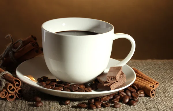 Kopje koffie en bonen, kaneelstokjes en chocolade op plundering op bruine achtergrond — Stockfoto