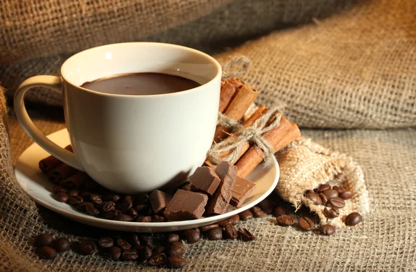 Чашка кофе и бобов, коричные палочки и шоколад на фоне мешка — стоковое фото